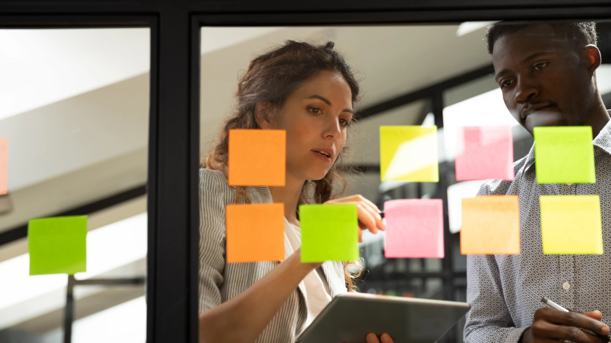 Two employees looking at sticky notes on pane of glass